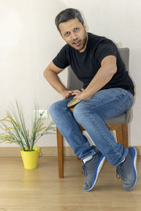 Portrait of man banging drum while sitting on chair at home