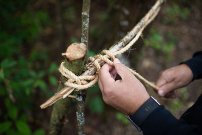 Man ties sticks together with twine to make tree fort.