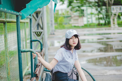 Portrait of young woman sitting on bench at basketball court