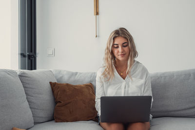 Young woman using laptop while sitting on sofa at home