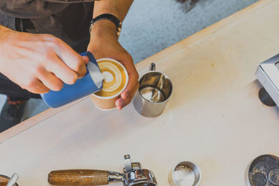 Cropped image of hand making froth art in espresso coffee at counter in cafe