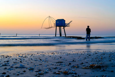 Silhouette people standing on beach against sky during sunset