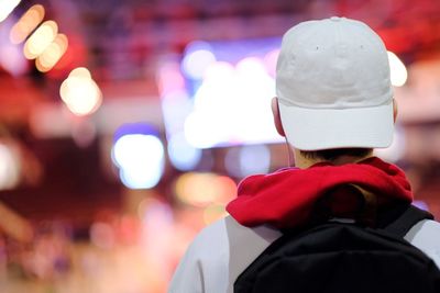 Rear view of man wearing hat standing against illuminated city