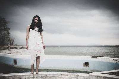 Portrait of woman standing by swimming pool against sky