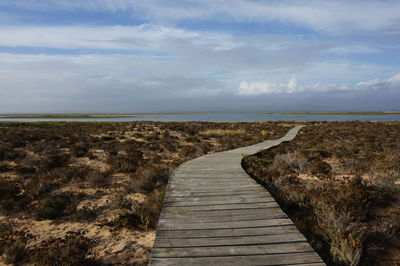 Boardwalk leading towards sea against sky