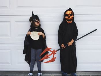 Girl and boy in halloween costume standing against wall