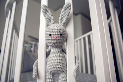 Grey knitted rabbit sitting behind the partitions in bed