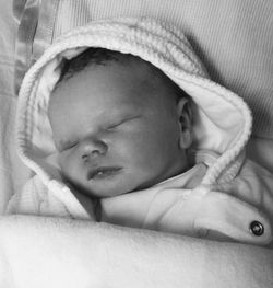High angle view of newborn baby wearing hooded shirt while sleeping on bed