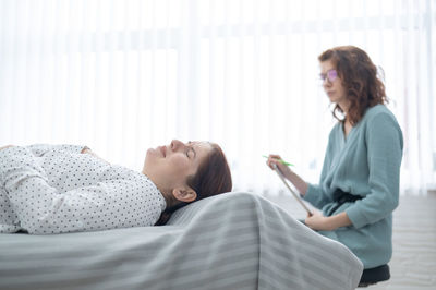 Side view of woman using digital tablet while sitting on bed at home