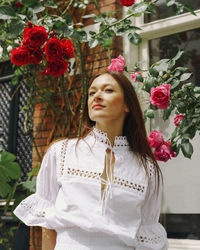 Portrait of young woman standing amidst red roses