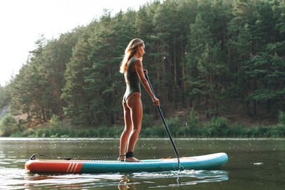 The young woman in green sweemsuit on sup boat with oar floating on river, weekend trip and travel