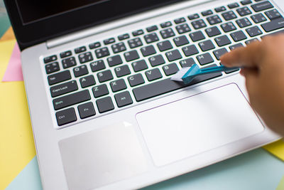 Cropped hand cleaning laptop with brush at table