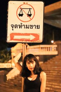 Young woman standing against road sign in city at night