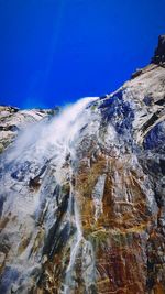 Low angle view of waterfall against clear blue sky