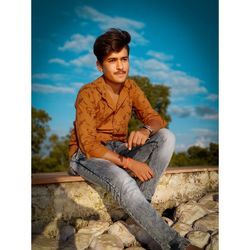 Young man sitting on rock against sky