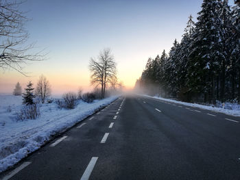 Snow covered road against sky during sunset