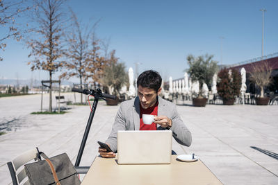 Full length of man using phone while sitting on table