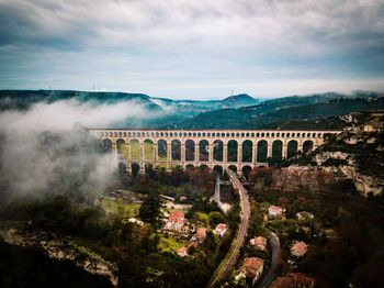 Arch bridge over mountain against cloudy sky