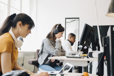 Side view of focused programmers using laptops on desk while sitting in office