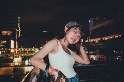 Portrait of young woman against illuminated city at night