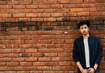 Portrait of young man standing against brick wall