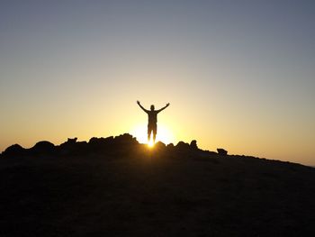 Silhouette man with arms outstretched standing on land against sky during sunset