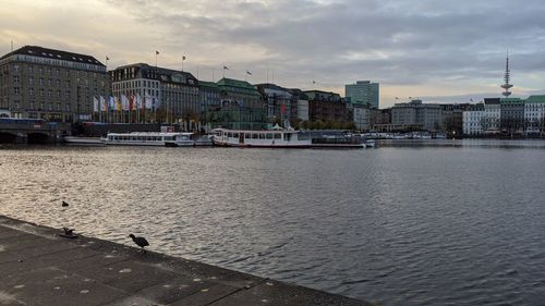 View of buildings by river against cloudy sky