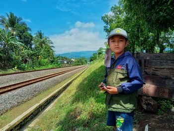 Portrait of young man standing on railroad track against sky