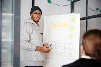 Male entrepreneur giving presentation over whiteboard during meeting in office