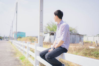 Side view of young man sitting on railing