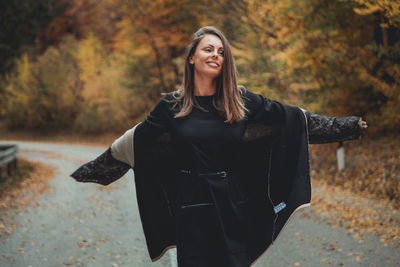 Smiling woman standing on road against trees during autumn