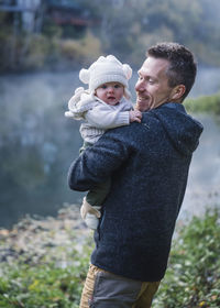 A man is holding a baby near a river