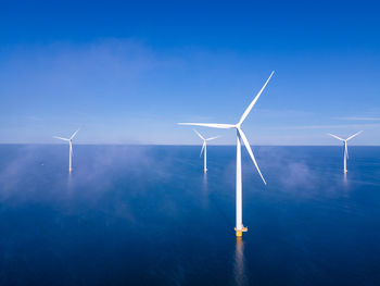 Wind turbines in sea against blue sky