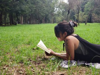 Side view of woman reading book on field