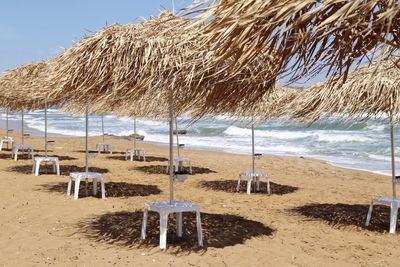 Beach parasols made of palm leaves against blue sky on a windy but sunny beach by the sea ,no people