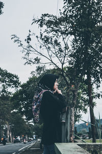 Side view of young man standing against trees