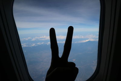 Person hand against sky seen through window