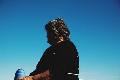 Side view of woman sitting against blue sky during sunny day