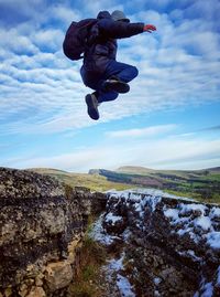 Man jumping over rocks against sky