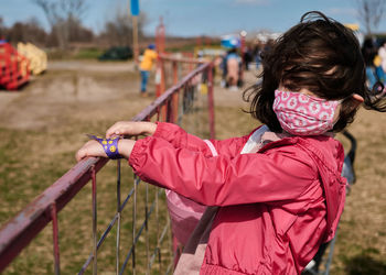 Girl in a mask standing on a wire fence at the county fair