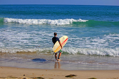 Rear view of woman holding surfboard on shore at beach