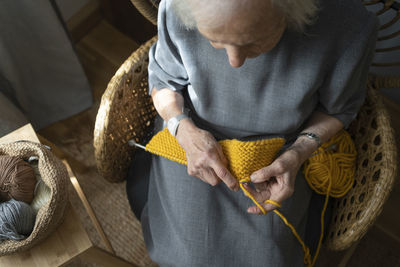 Senior woman knitting on chair at home