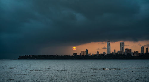 Scenic view of sea by buildings against sky at sunset