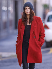 Portrait of young woman walking with hands in pockets on road