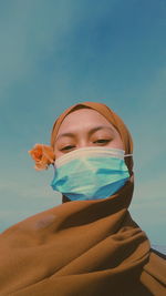 Low angle portrait of woman wearing mask and hijab against sky
