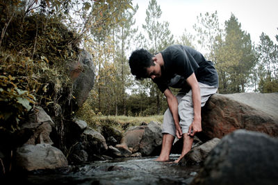 Side view of young man on rock against trees