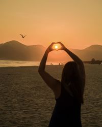 Silhouette woman standing by sea against sky during sunset