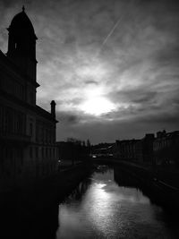 Bridge over river by buildings against sky at dusk