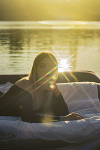 Young woman lies on a mattress on the water and the sunset reflects off the water with rays of light