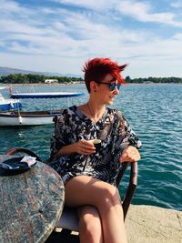 Smiling woman sitting at table by sea against sky